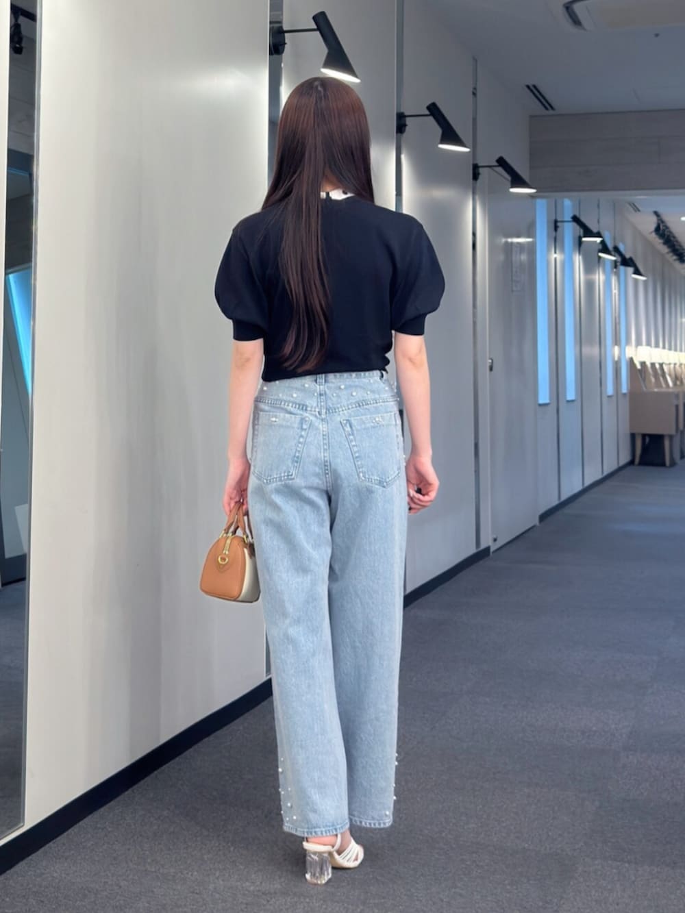 ブラウン系のハンドバッグ、ブルー系のデニムパンツ、ホワイト系のサンダルを着用したレディースの夏コーディネートの4枚目の写真