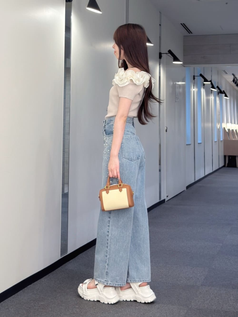 ブラウン系のハンドバッグ、ブルー系のデニムパンツ、ホワイト系のサンダルを着用したレディースの夏コーディネートの3枚目の写真
