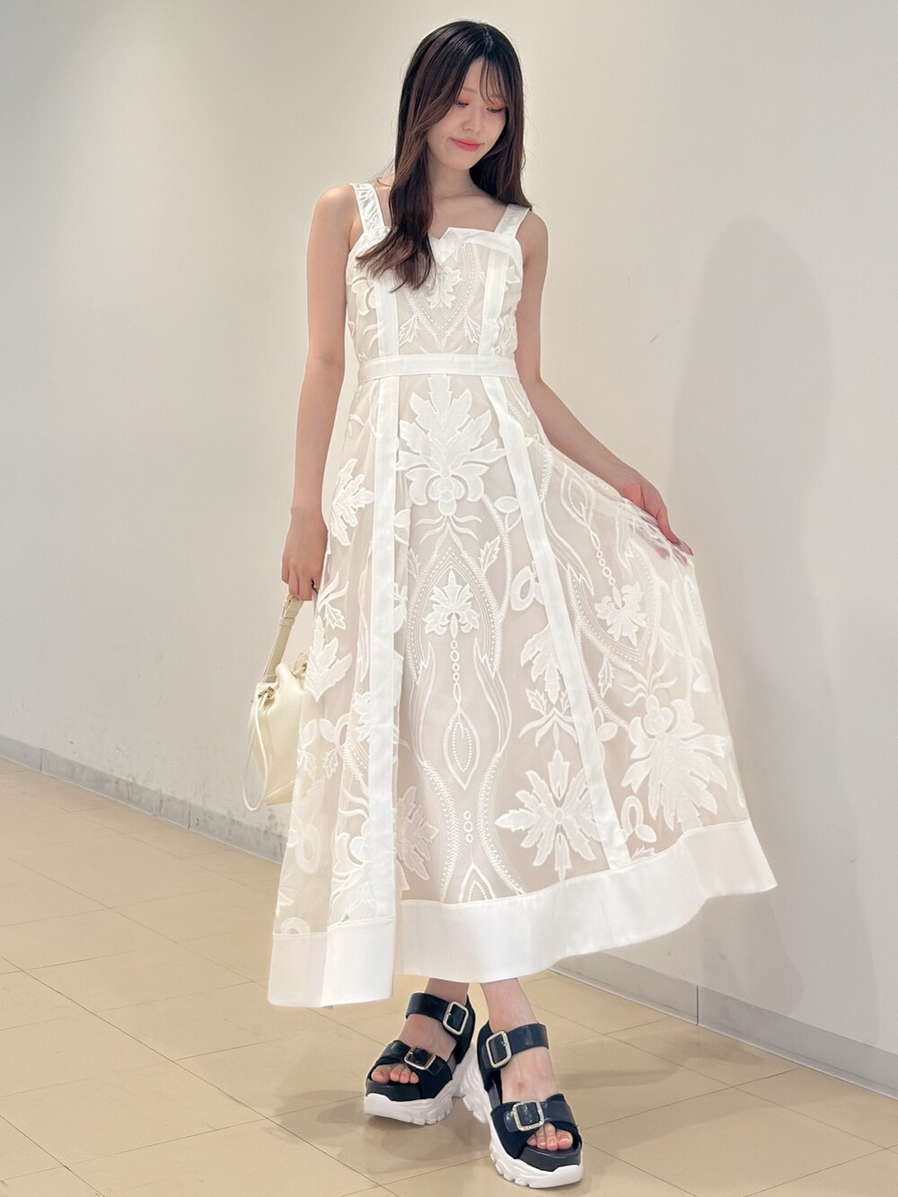 ホワイト系のワンピース、ホワイト系のハンドバッグ、ブラック系のサンダルを着用したレディースの夏コーディネートの3枚目の写真