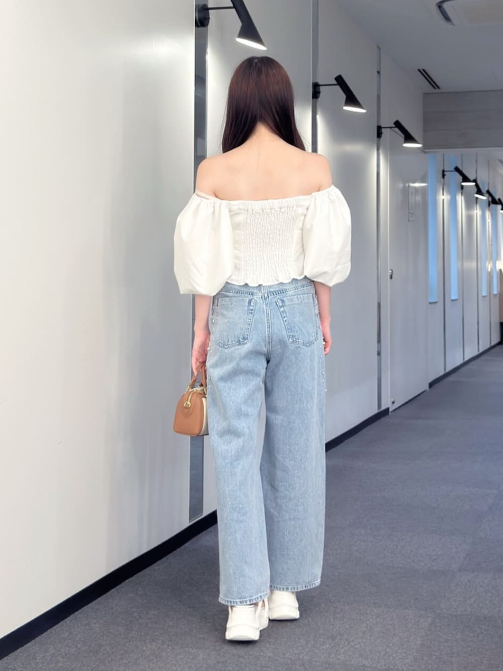 ブラウン系のハンドバッグ、ブルー系のデニムパンツ、ホワイト系のサンダルを着用したレディースの夏コーディネートの4枚目の写真