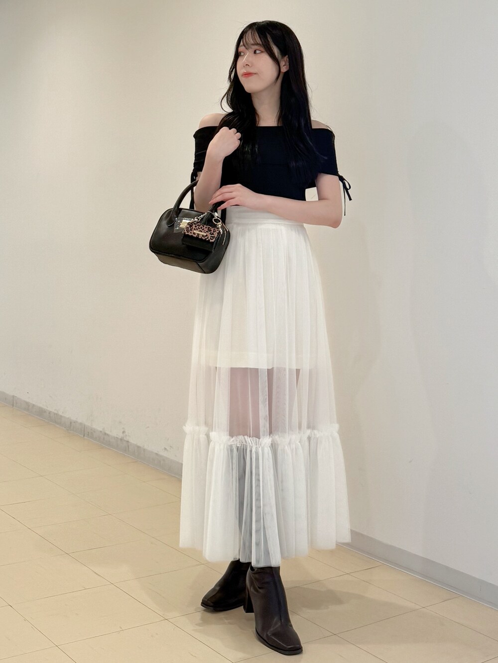 ブラック系のニット/セーター、ホワイト系のスカート、ブラック系のハンドバッグを着用したレディースの夏コーディネートの2枚目の写真