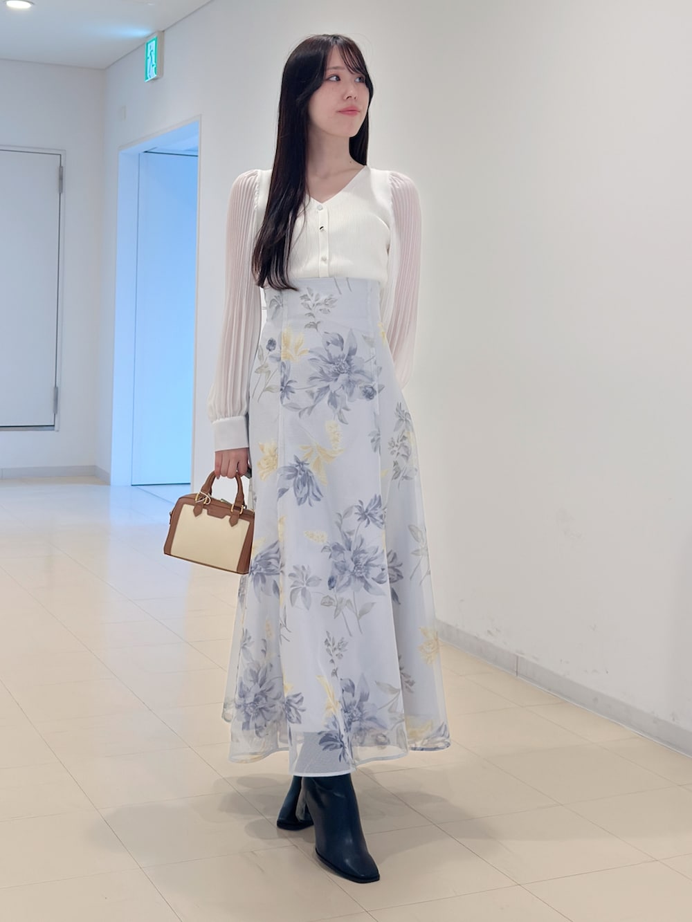 ホワイト系のニット/セーター、グリーン系のスカート、ブラウン系のハンドバッグを着用したレディースの冬コーディネートの2枚目の写真