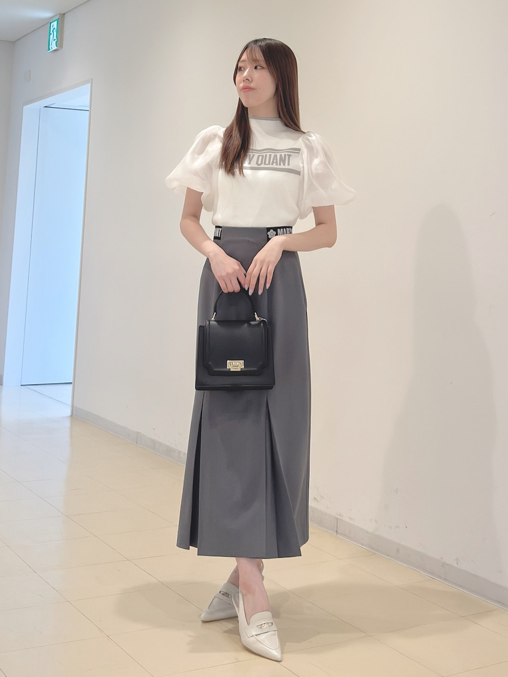 ホワイト系のニット/セーター、グレー系のスカート、ブラック系のハンドバッグを着用したレディースの春コーディネートの2枚目の写真