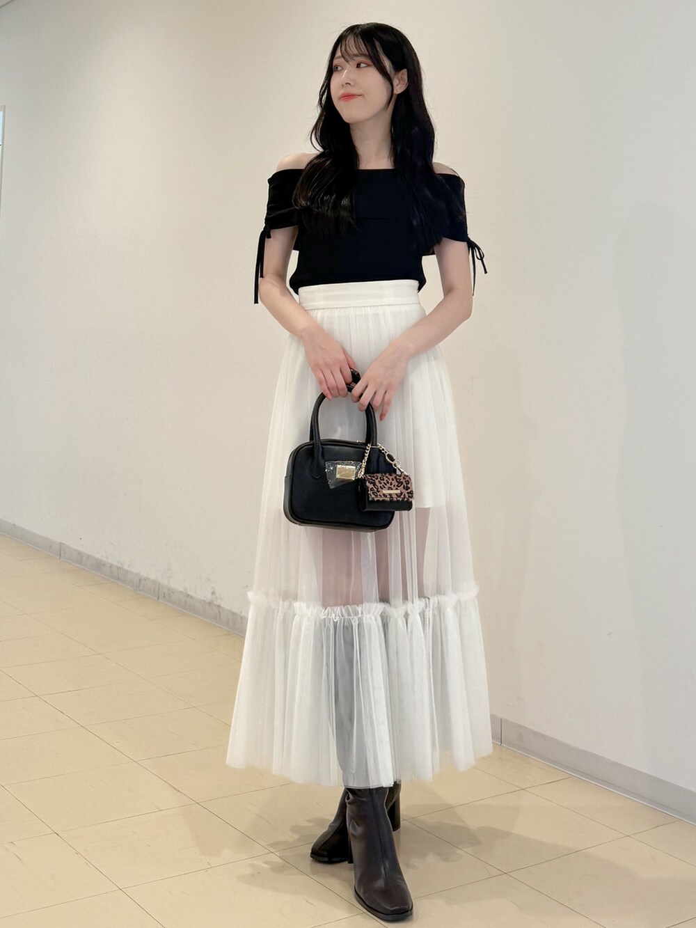 ブラック系のニット/セーター、ホワイト系のスカート、ブラック系のハンドバッグを着用したレディースの夏コーディネートの3枚目の写真