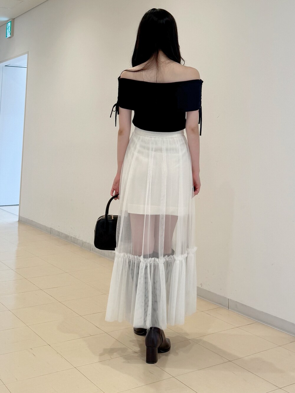 ブラック系のニット/セーター、ホワイト系のスカート、ブラック系のハンドバッグを着用したレディースの夏コーディネートの5枚目の写真