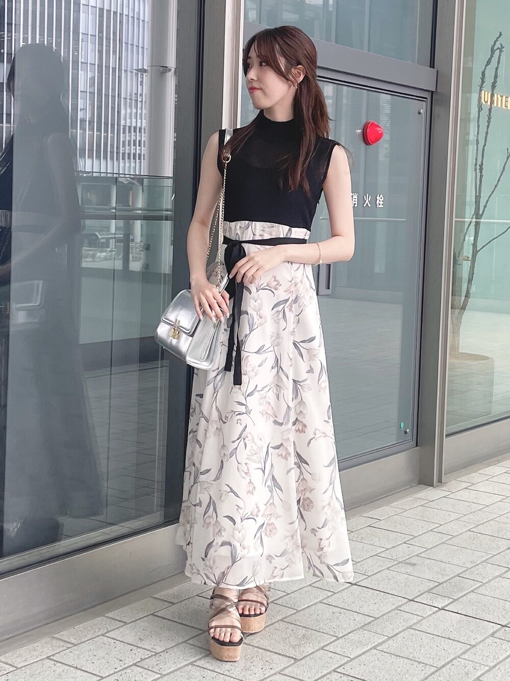 シルバー系のハンドバッグ、ブラック系のワンピース、ブラック系のサンダルを着用したレディースの春コーディネートの2枚目の写真