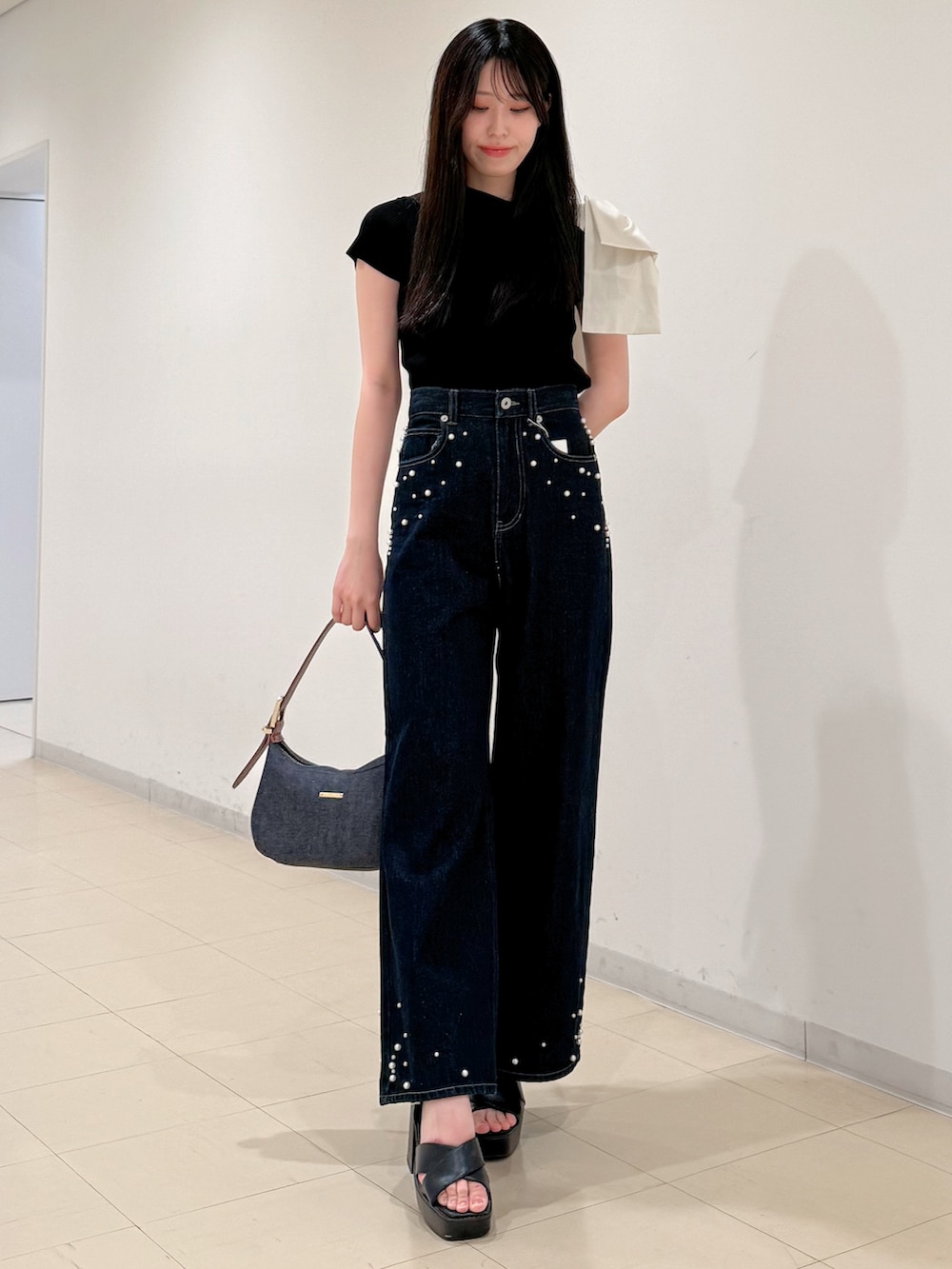 ブラック系のニット/セーター、ブルー系のデニムパンツ、ブルー系のショルダーバッグを着用したレディースの夏コーディネートの2枚目の写真