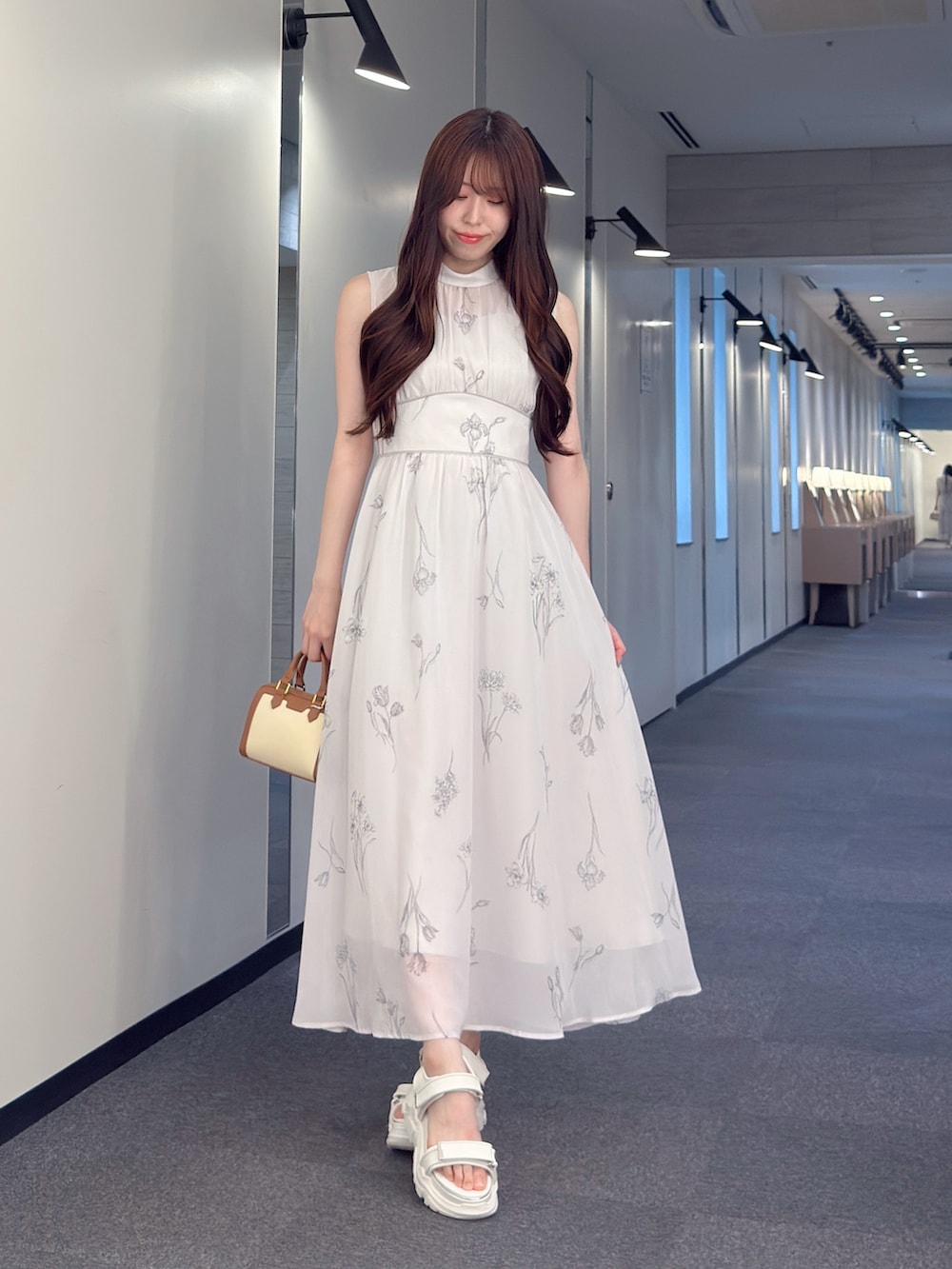 グレー系のワンピース、ブラウン系のハンドバッグ、ホワイト系のサンダルを着用したレディースの夏コーディネートの2枚目の写真