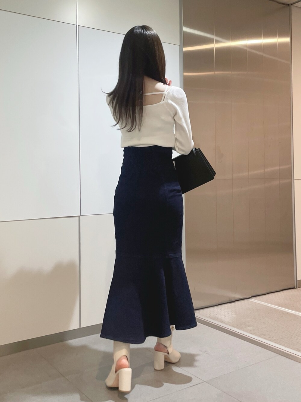 ブラック系のハンドバッグ、ホワイト系のニット/セーター、ブルー系のデニムスカートを着用したレディースの冬コーディネートの4枚目の写真