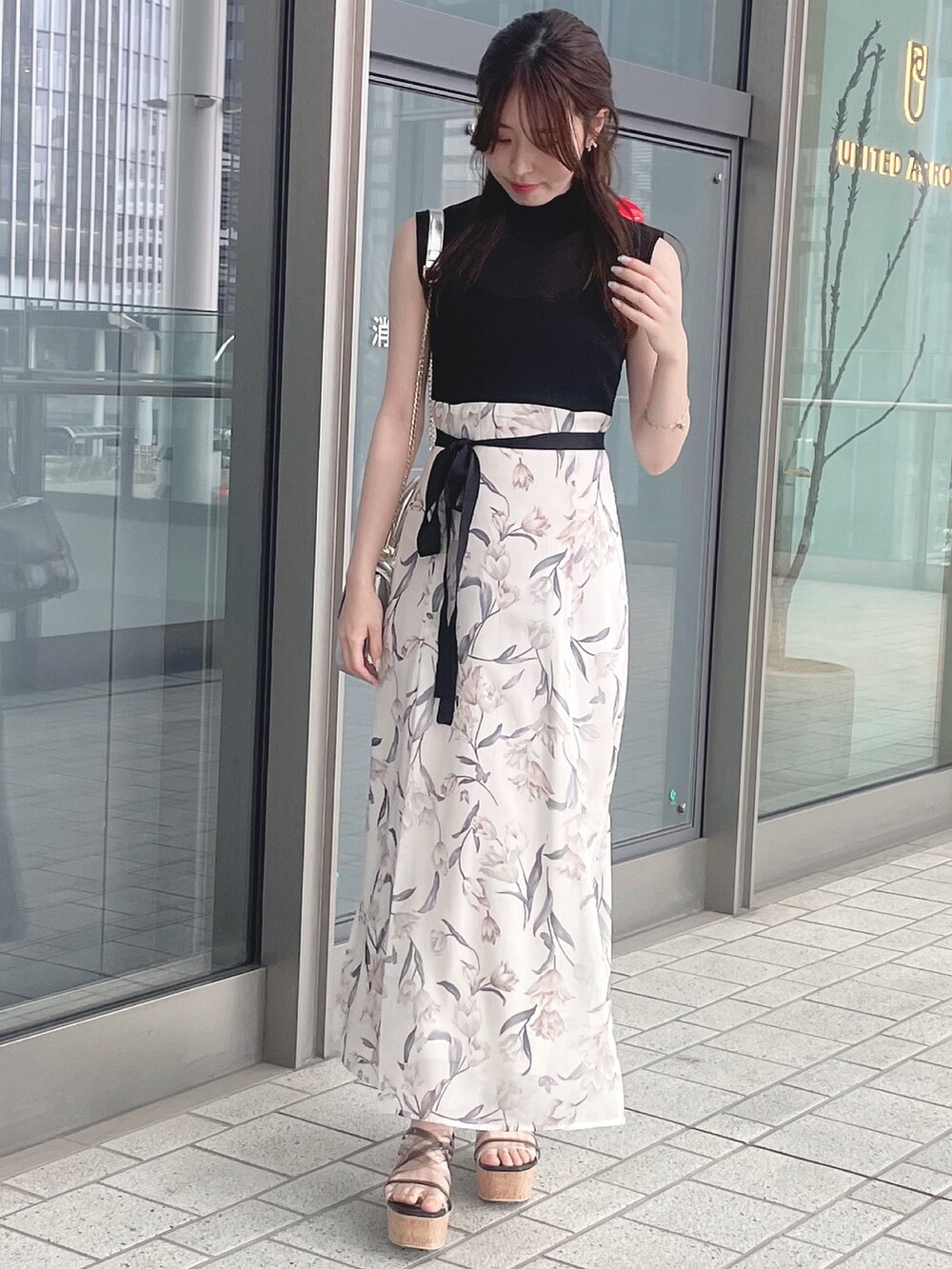 シルバー系のハンドバッグ、ブラック系のワンピース、ブラック系のサンダルを着用したレディースの春コーディネートの3枚目の写真