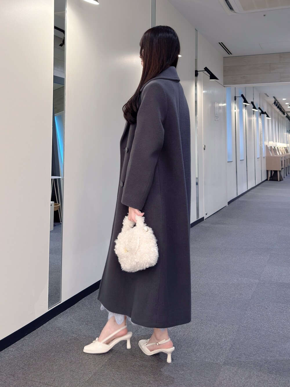 グレー系のチェスターコート、ブルー系のワンピース、ホワイト系のハンドバッグを着用したレディースの秋コーディネートの3枚目の写真