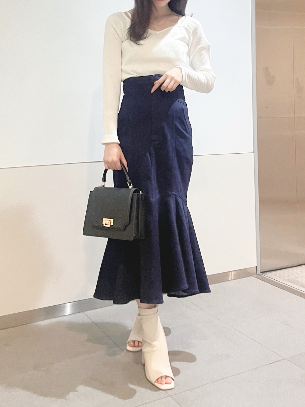 ブラック系のハンドバッグ、ホワイト系のニット/セーター、ブルー系のデニムスカートを着用したレディースの冬コーディネートの2枚目の写真