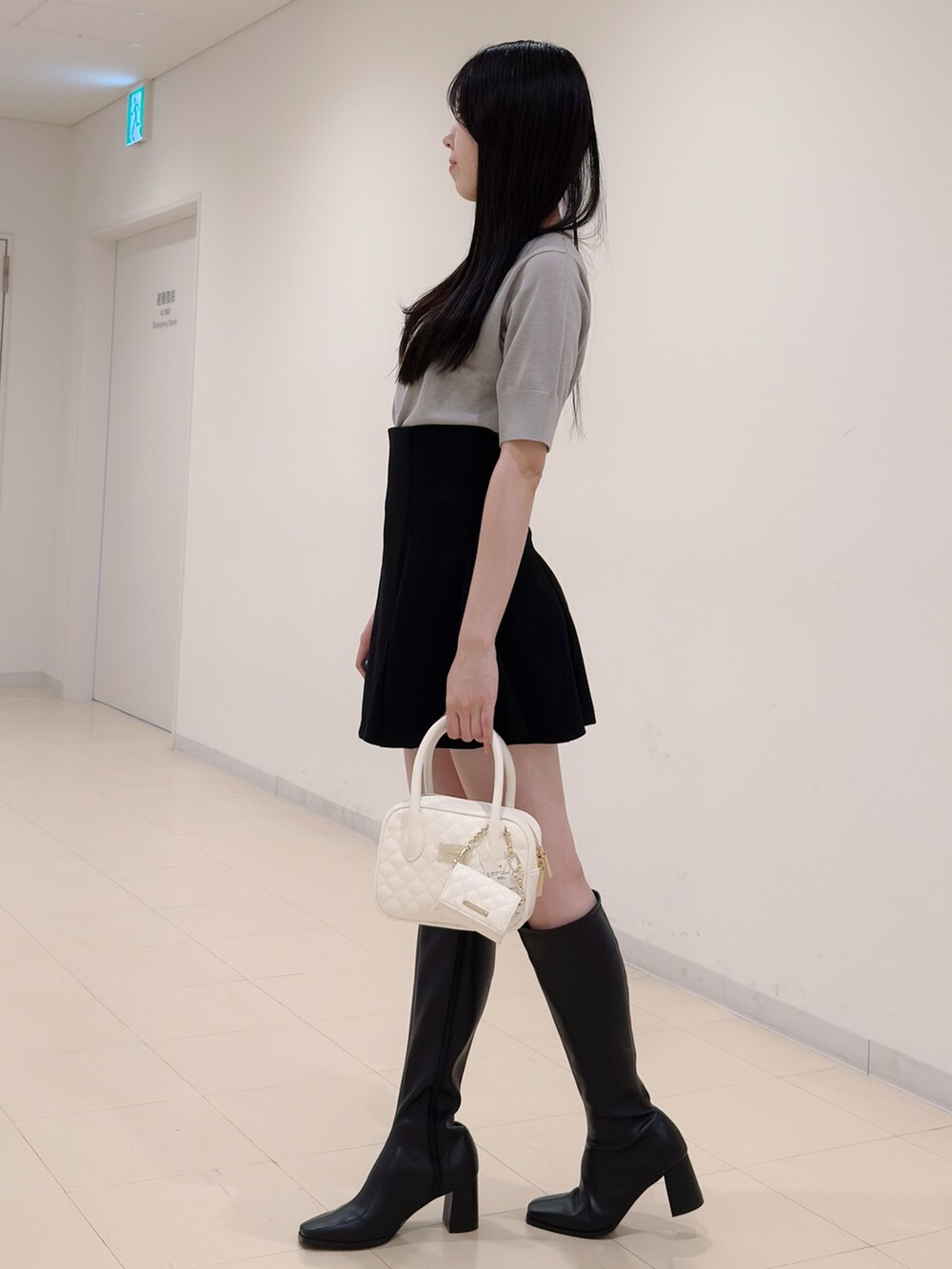 グレー系のニット/セーター、ブラック系のスカート、ホワイト系のハンドバッグを着用したレディースの秋コーディネートの3枚目の写真