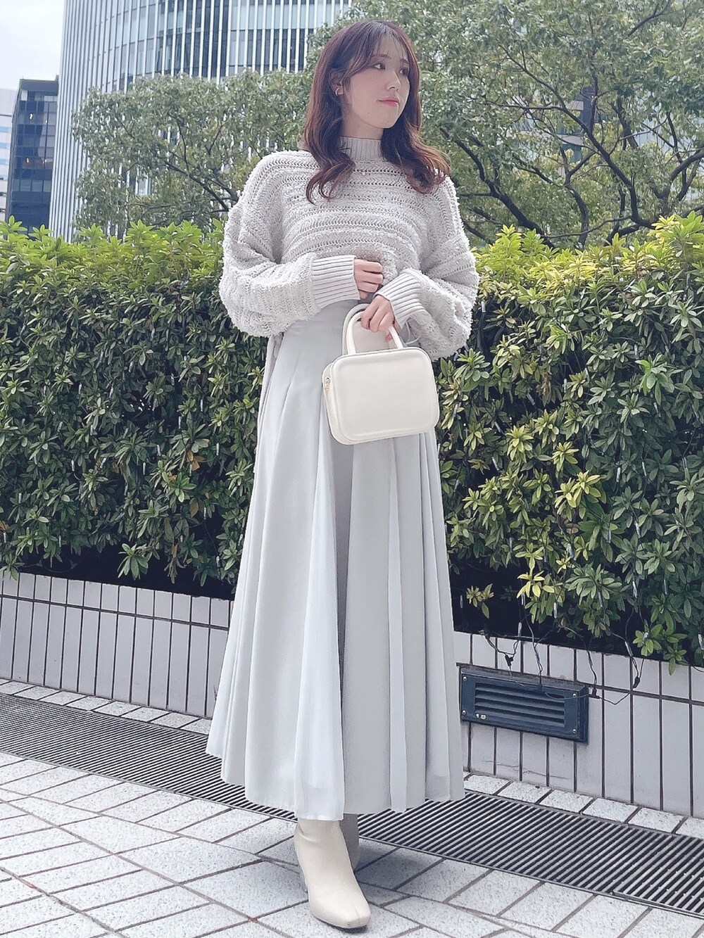 グレー系のニット/セーター、グリーン系のスカート、ホワイト系のハンドバッグを着用したレディースの冬コーディネートの2枚目の写真