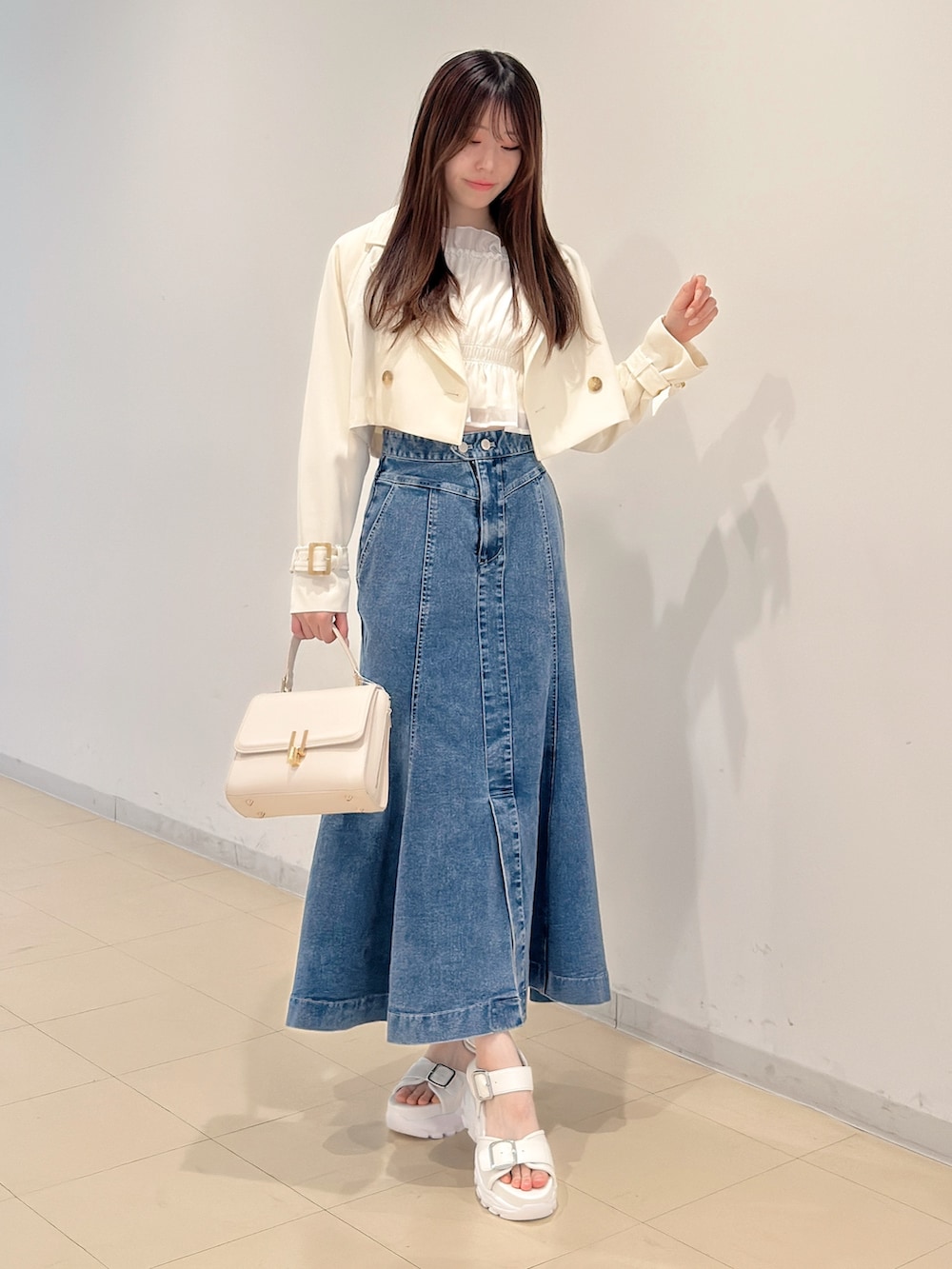ホワイト系のトレンチコート、ブルー系のスカート、ホワイト系のサンダルを着用したレディースの春コーディネートの2枚目の写真