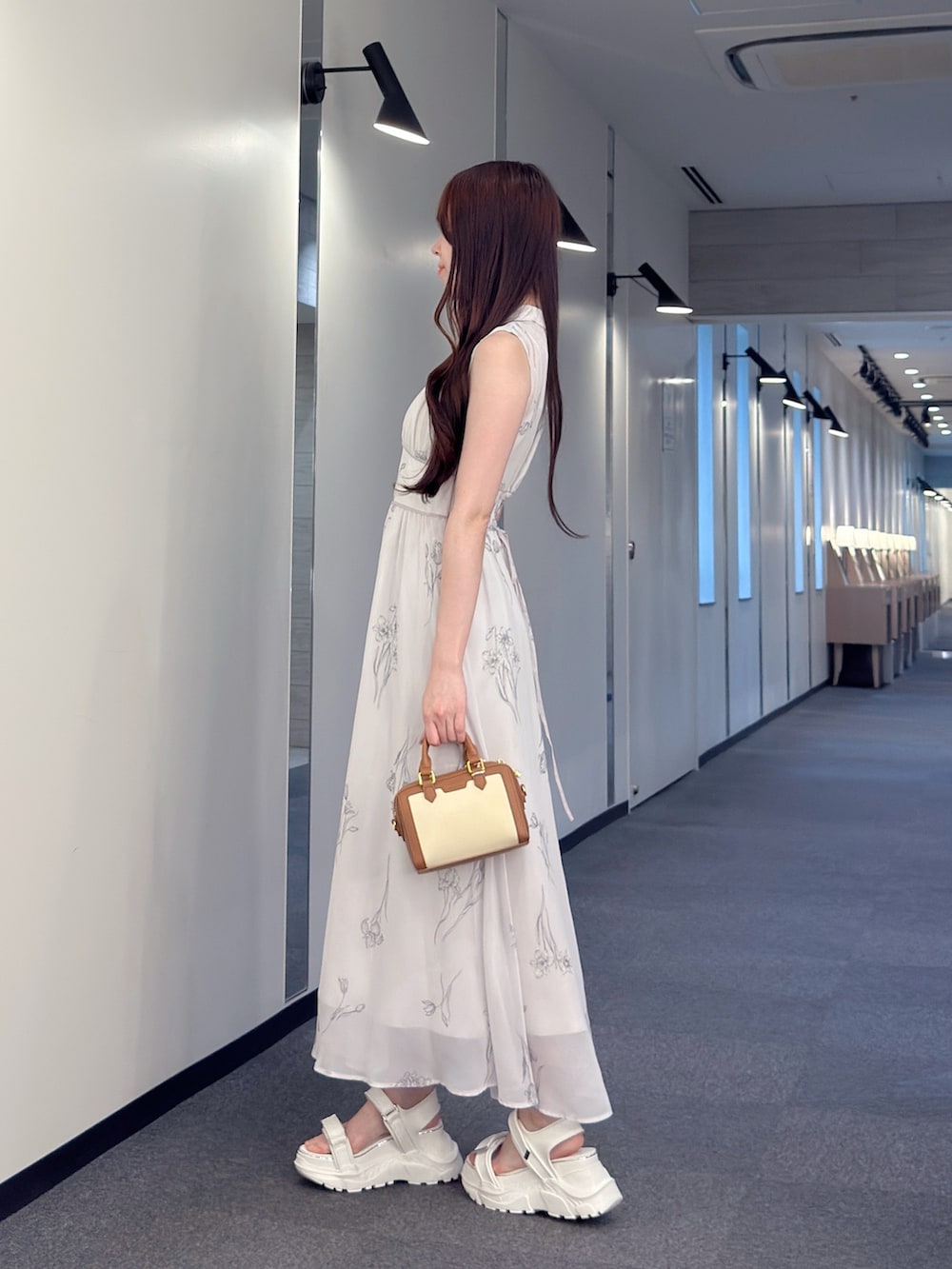 グレー系のワンピース、ブラウン系のハンドバッグ、ホワイト系のサンダルを着用したレディースの夏コーディネートの3枚目の写真