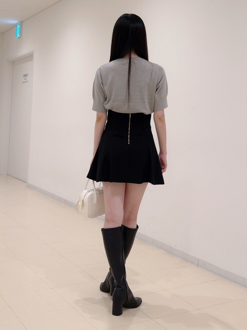 グレー系のニット/セーター、ブラック系のスカート、ホワイト系のハンドバッグを着用したレディースの秋コーディネートの4枚目の写真