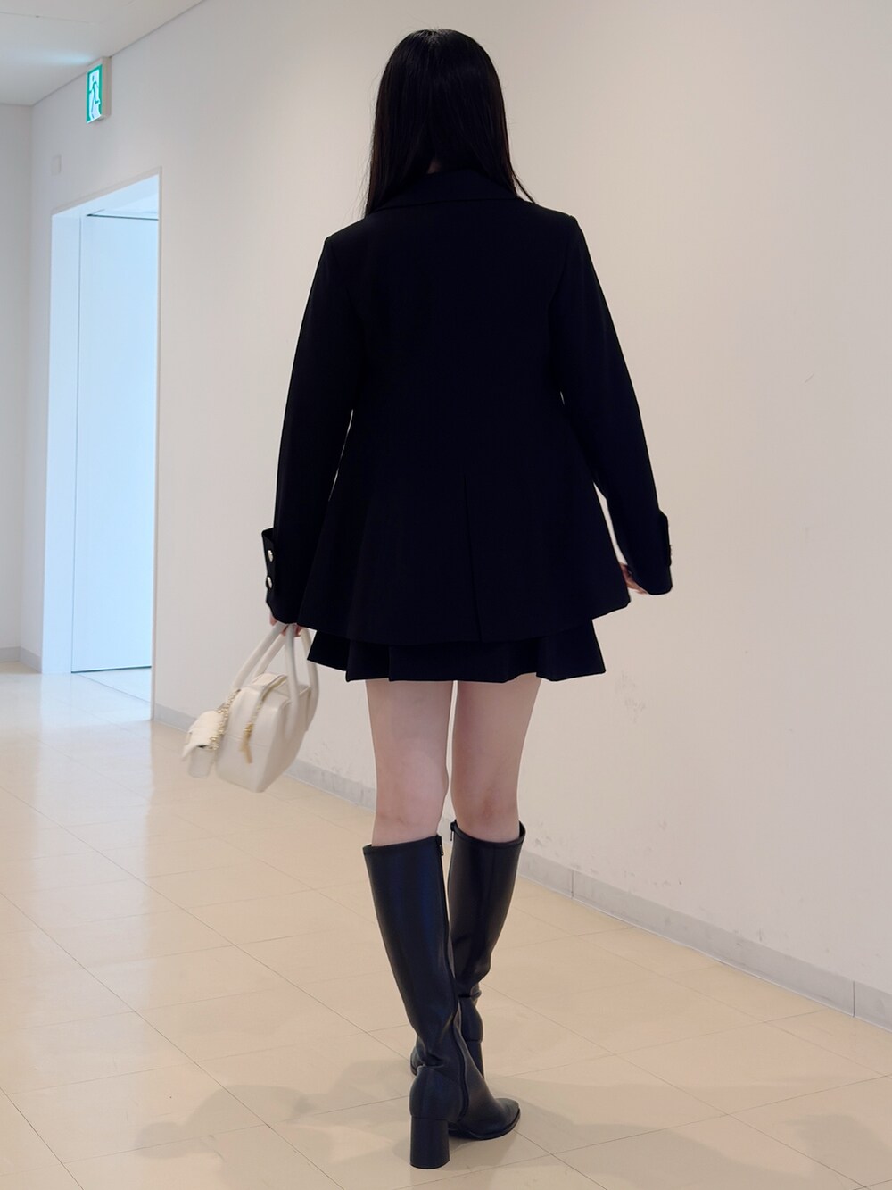 ブラック系のテーラードジャケット、グレー系のニット/セーター、ブラック系のスカートを着用したレディースの秋コーディネートの4枚目の写真