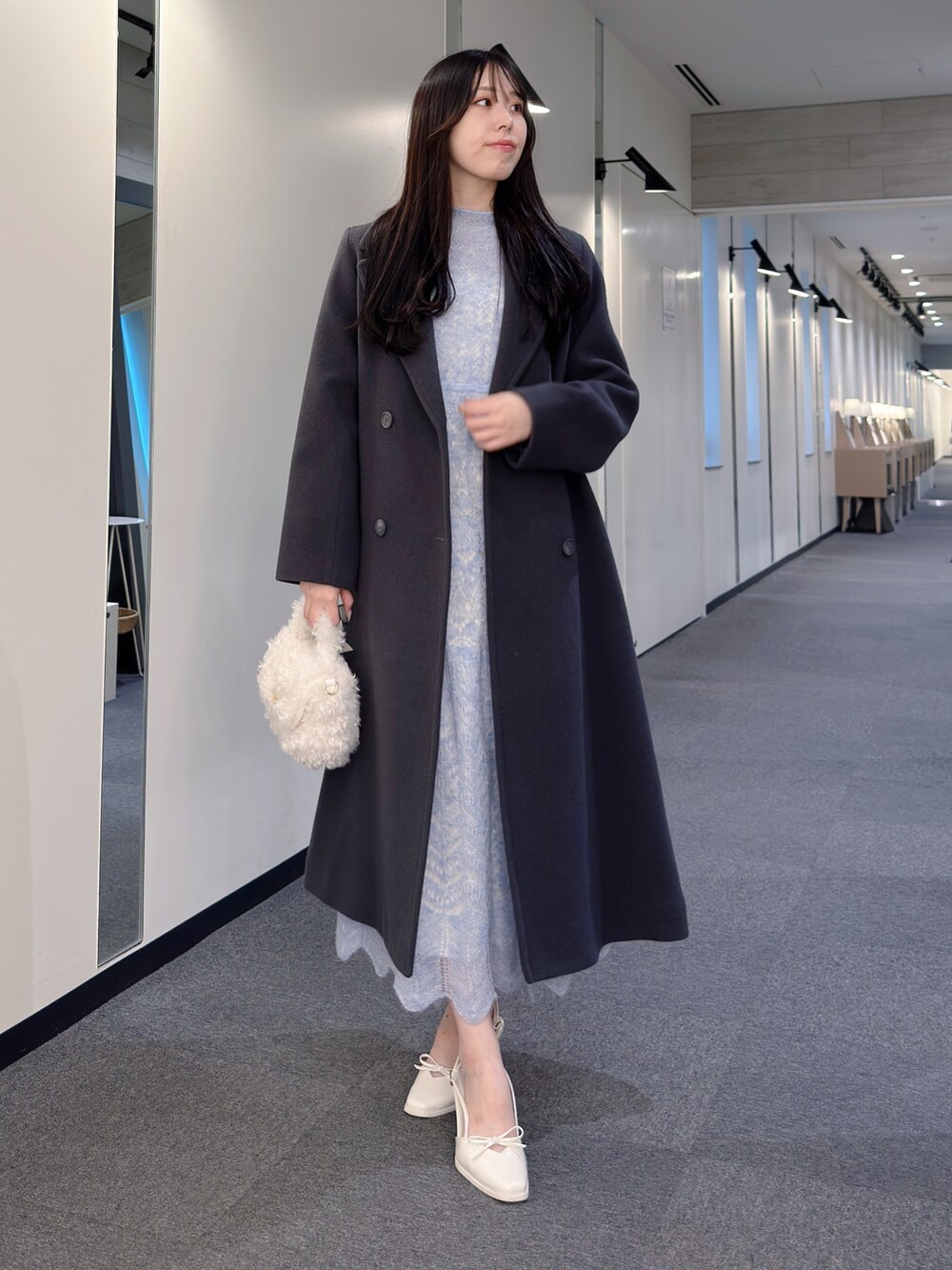 グレー系のチェスターコート、ブルー系のワンピース、ホワイト系のハンドバッグを着用したレディースの秋コーディネートの2枚目の写真