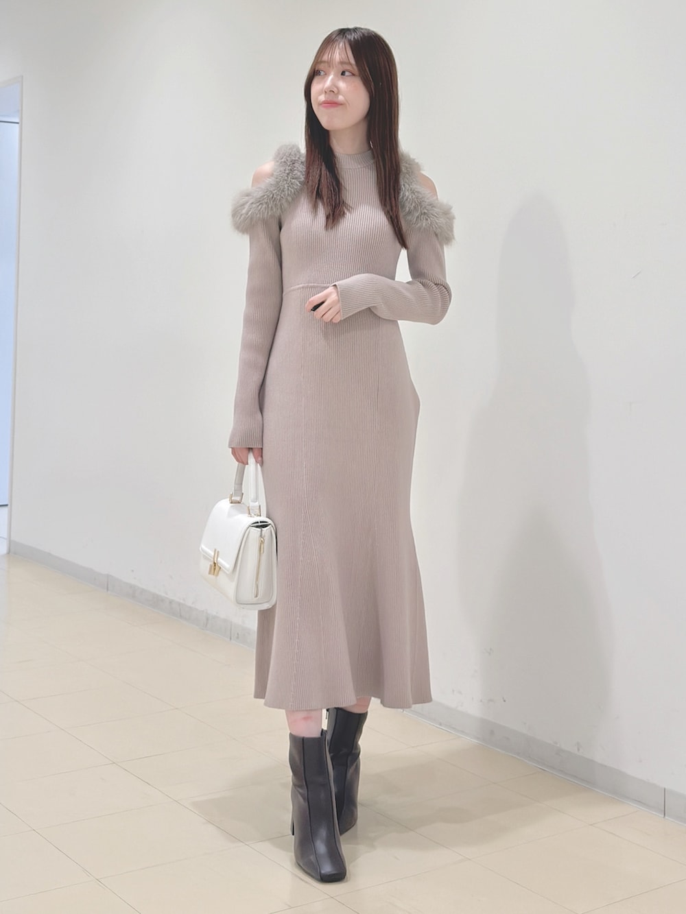ベージュ系のワンピース、ホワイト系のハンドバッグ、ブラウン系のブーツを着用したレディースの冬コーディネートの2枚目の写真