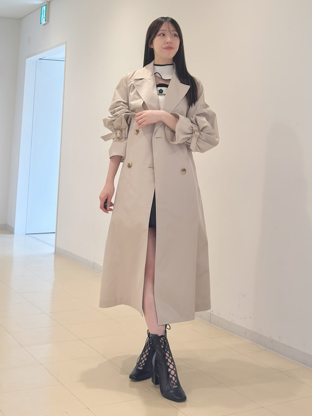 ベージュ系のトレンチコート、ホワイト系のニット/セーター、ブラック系のスカートを着用したレディースの春コーディネートの2枚目の写真
