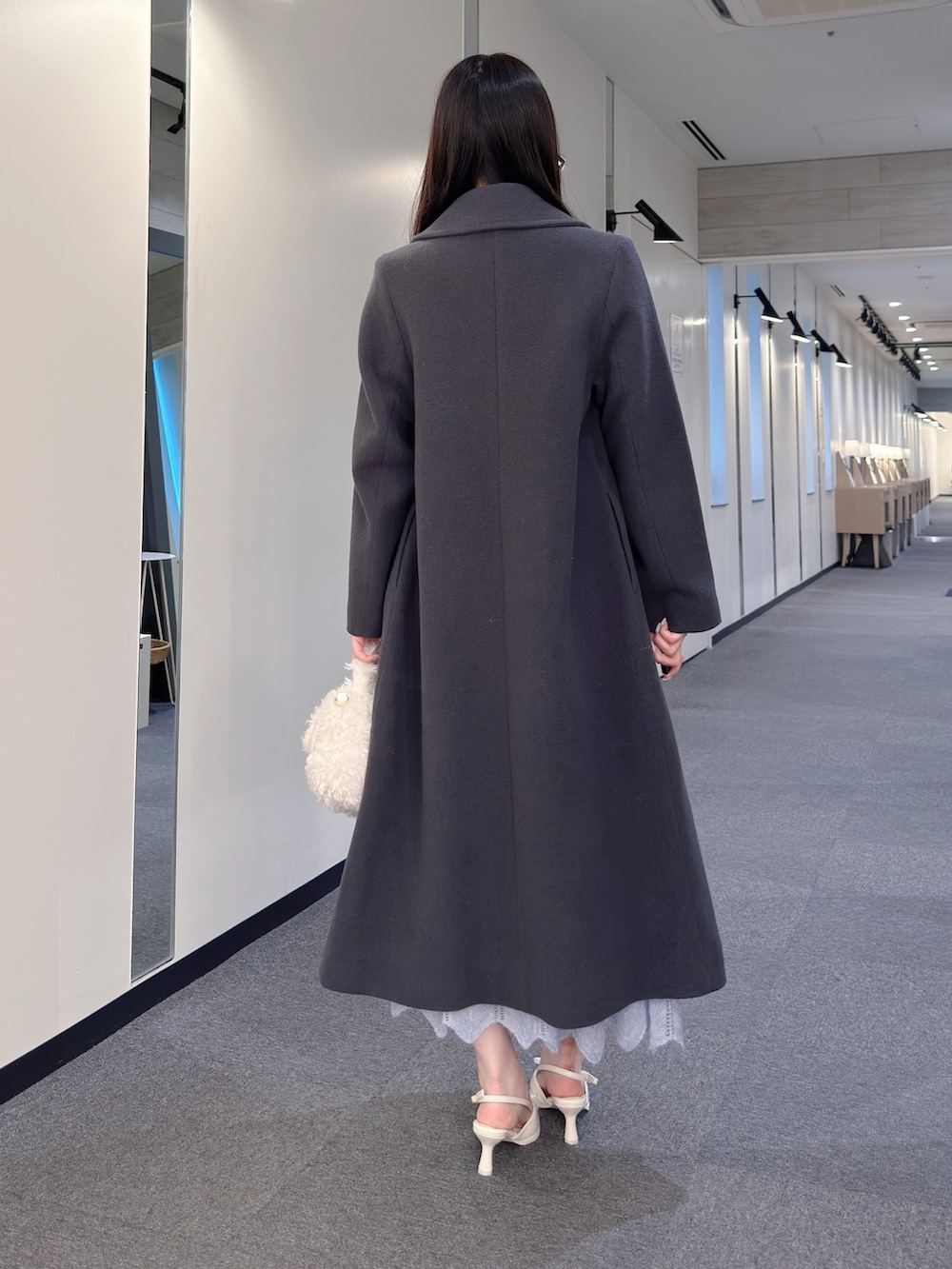 グレー系のチェスターコート、ブルー系のワンピース、ホワイト系のハンドバッグを着用したレディースの秋コーディネートの4枚目の写真