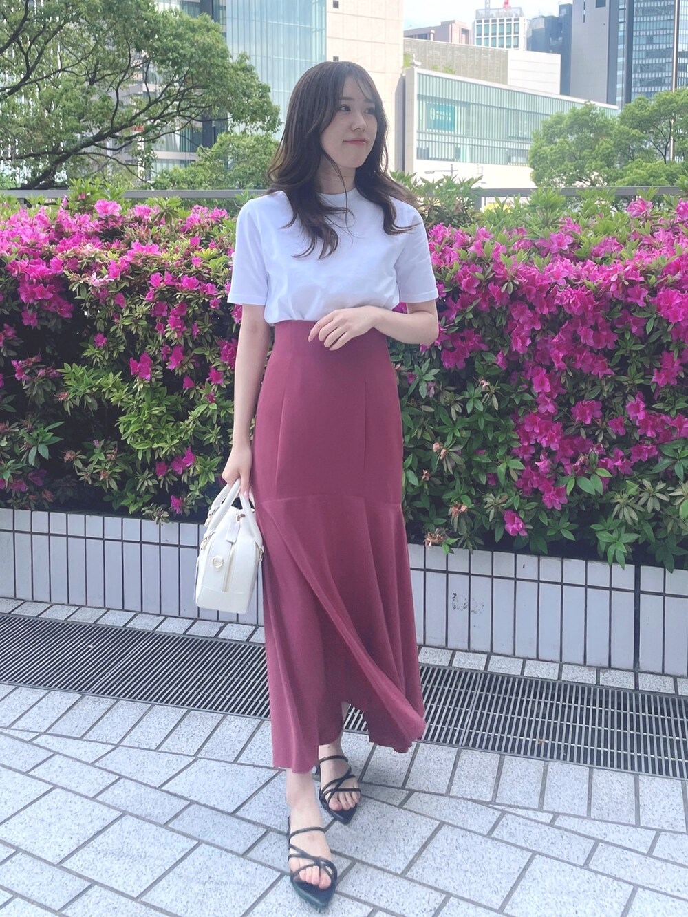 ピンク系のスカート、ホワイト系のTシャツ/カットソー、ブラック系のサンダルを着用したレディースの春コーディネートの2枚目の写真