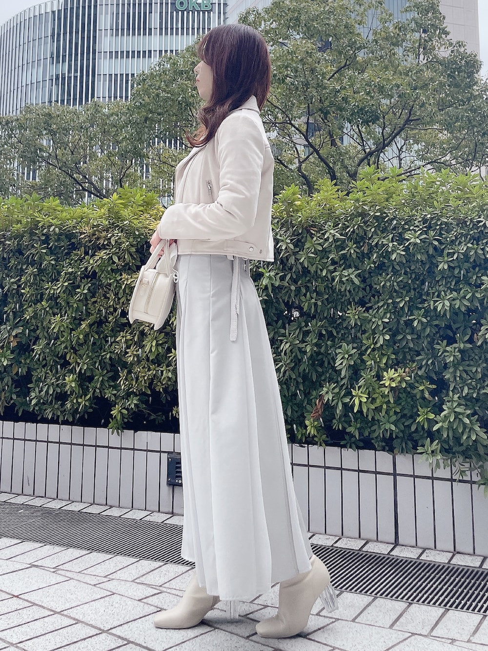 ピンク系のライダースジャケット、グレー系のニット/セーター、グリーン系のスカートを着用したレディースの冬コーディネートの3枚目の写真