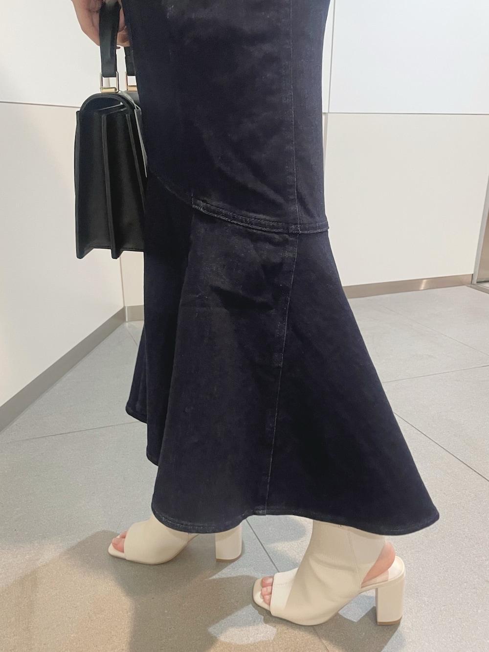 ブラック系のハンドバッグ、ホワイト系のニット/セーター、ブルー系のデニムスカートを着用したレディースの冬コーディネートの5枚目の写真