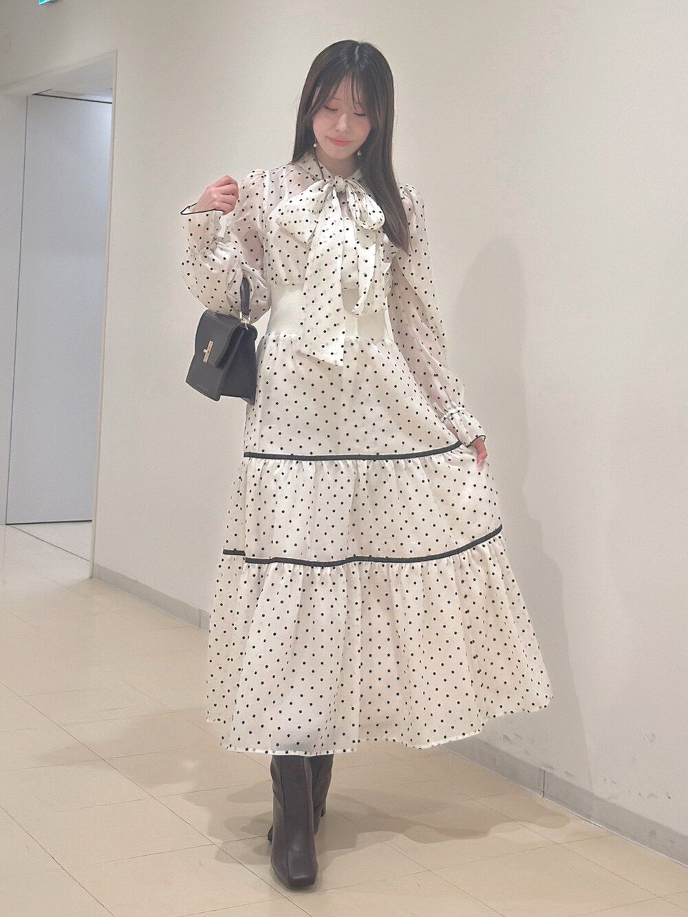 ホワイト系のワンピース、ブラウン系のハンドバッグ、ブラウン系のブーツを着用したレディースの冬コーディネートの2枚目の写真