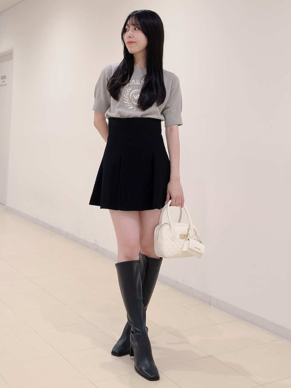 グレー系のニット/セーター、ブラック系のスカート、ホワイト系のハンドバッグを着用したレディースの秋コーディネートの2枚目の写真