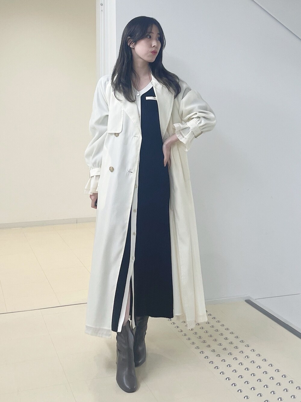 ホワイト系のトレンチコート、ブラック系のワンピース、ブラウン系のブーツを着用したレディースの冬コーディネートの2枚目の写真