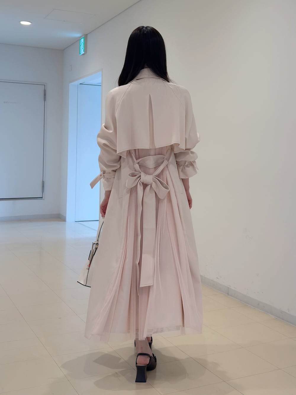 ピンク系のトレンチコート、ベージュ系のワンピース、ホワイト系のショルダーバッグを着用したレディースの冬コーディネートの3枚目の写真