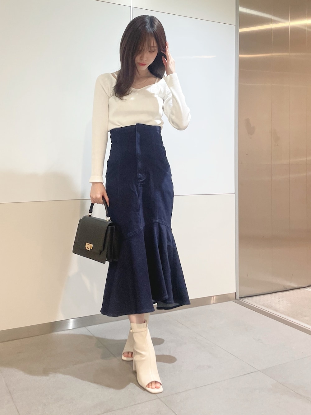 ブラック系のハンドバッグ、ホワイト系のニット/セーター、ブルー系のデニムスカートを着用したレディースの冬コーディネートの3枚目の写真