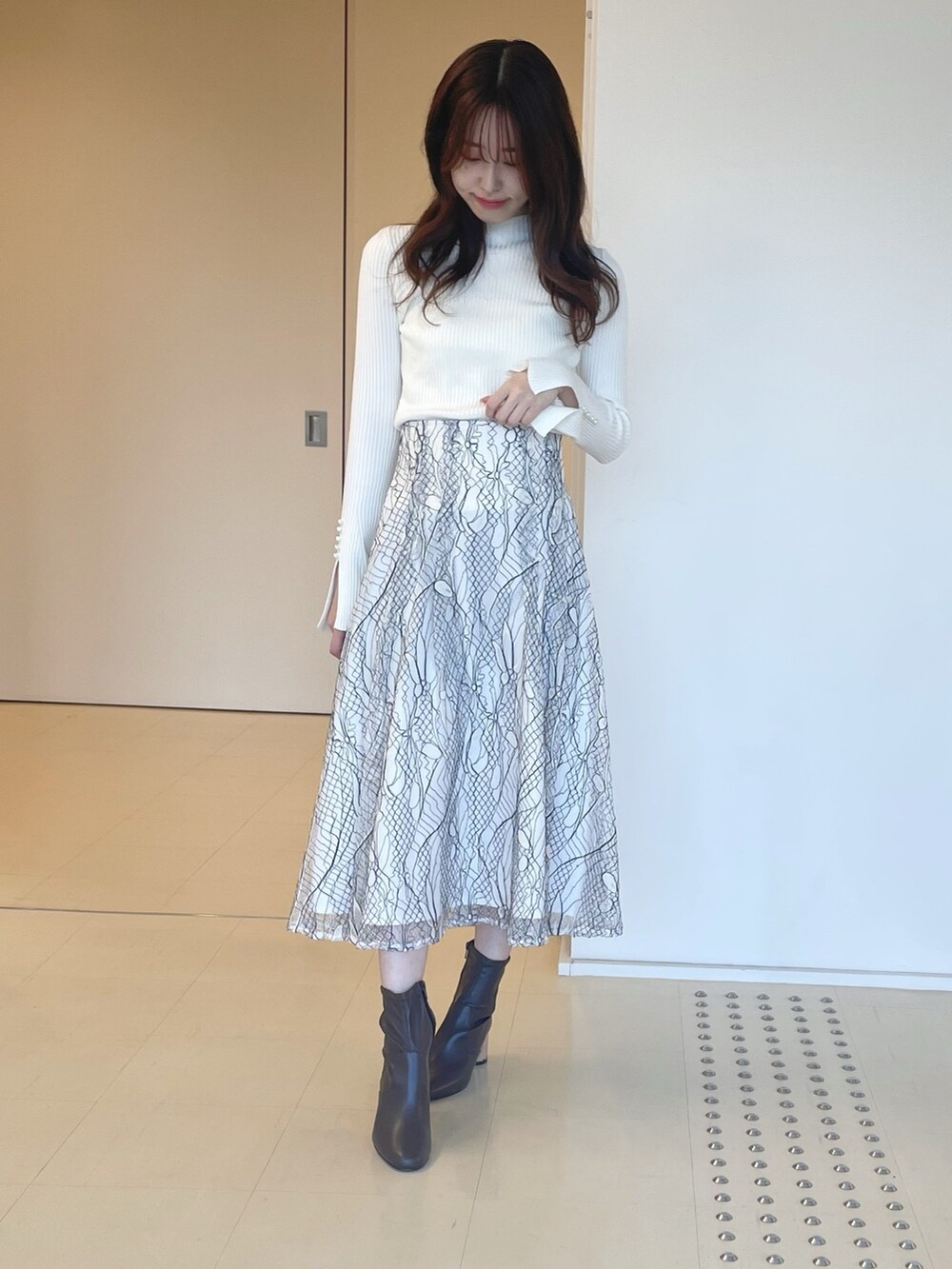 ベージュ系のトレンチコート、ホワイト系のニット/セーター、ホワイト系のスカートを着用したレディースの冬コーディネートの3枚目の写真