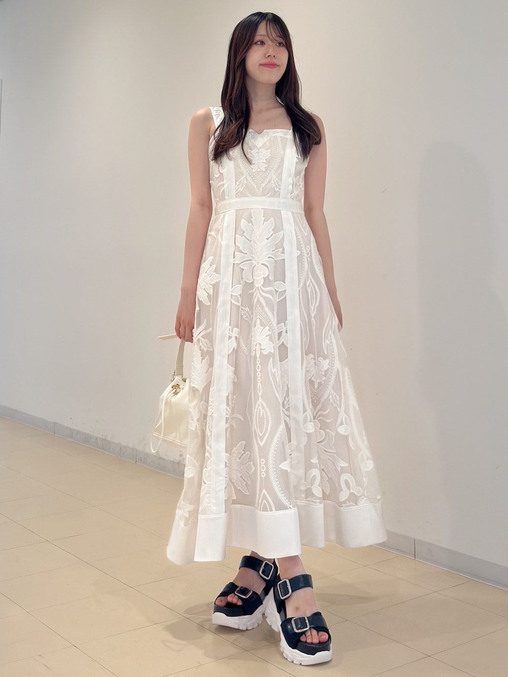 ホワイト系のワンピース、ホワイト系のハンドバッグ、ブラック系のサンダルを着用したレディースの夏コーディネートの2枚目の写真