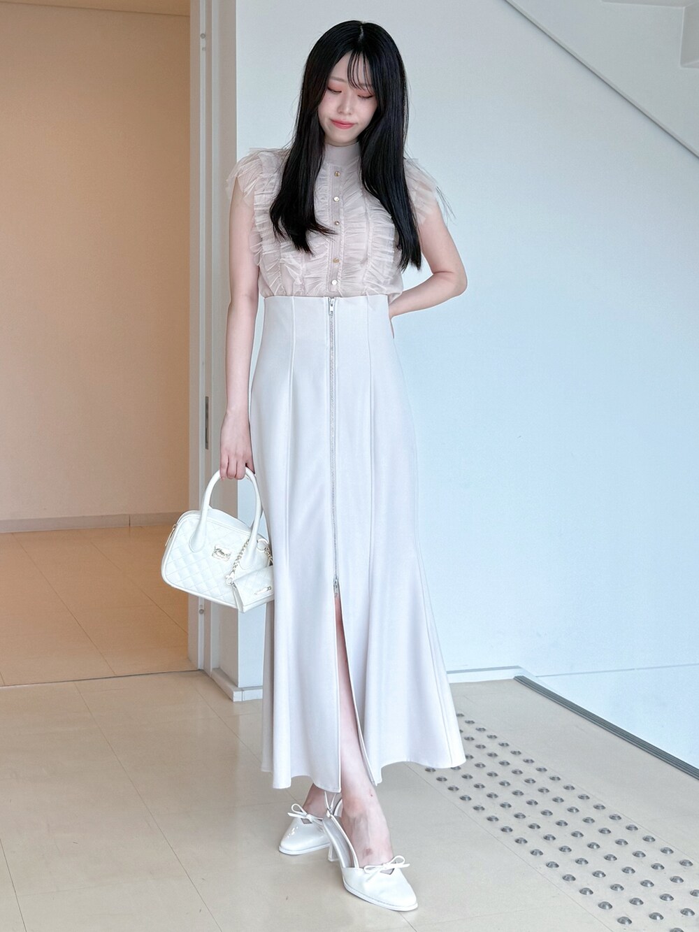 ピンク系のニット/セーター、グレー系のスカート、ホワイト系のハンドバッグを着用したレディースの夏コーディネートの2枚目の写真