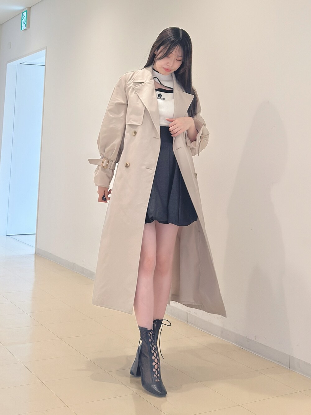ベージュ系のトレンチコート、ホワイト系のニット/セーター、ブラック系のスカートを着用したレディースの春コーディネートの6枚目の写真