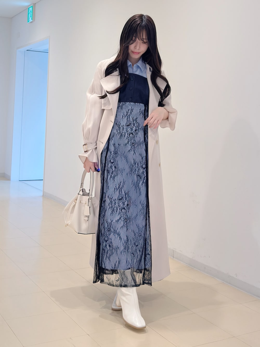 ホワイト系のトレンチコート、ブルー系のワンピース、ホワイト系のブーツを着用したレディースの冬コーディネートの2枚目の写真