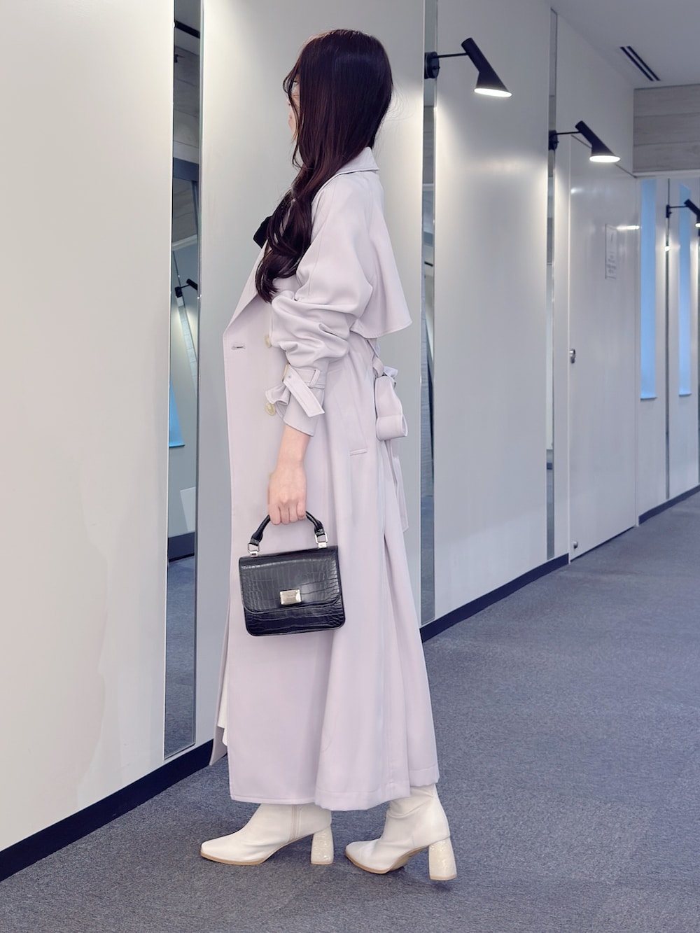 パープル系のトレンチコート、ホワイト系のワンピース、ブラック系のハンドバッグを着用したレディースの冬コーディネートの3枚目の写真
