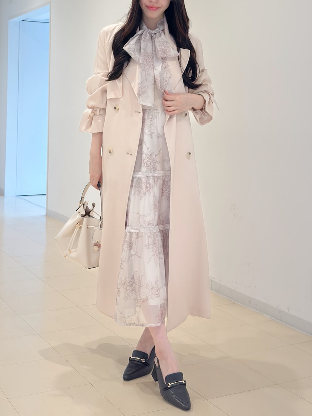 ピンク系のトレンチコート、ベージュ系のワンピース、ホワイト系のショルダーバッグを着用したレディースの冬コーディネートの2枚目の写真