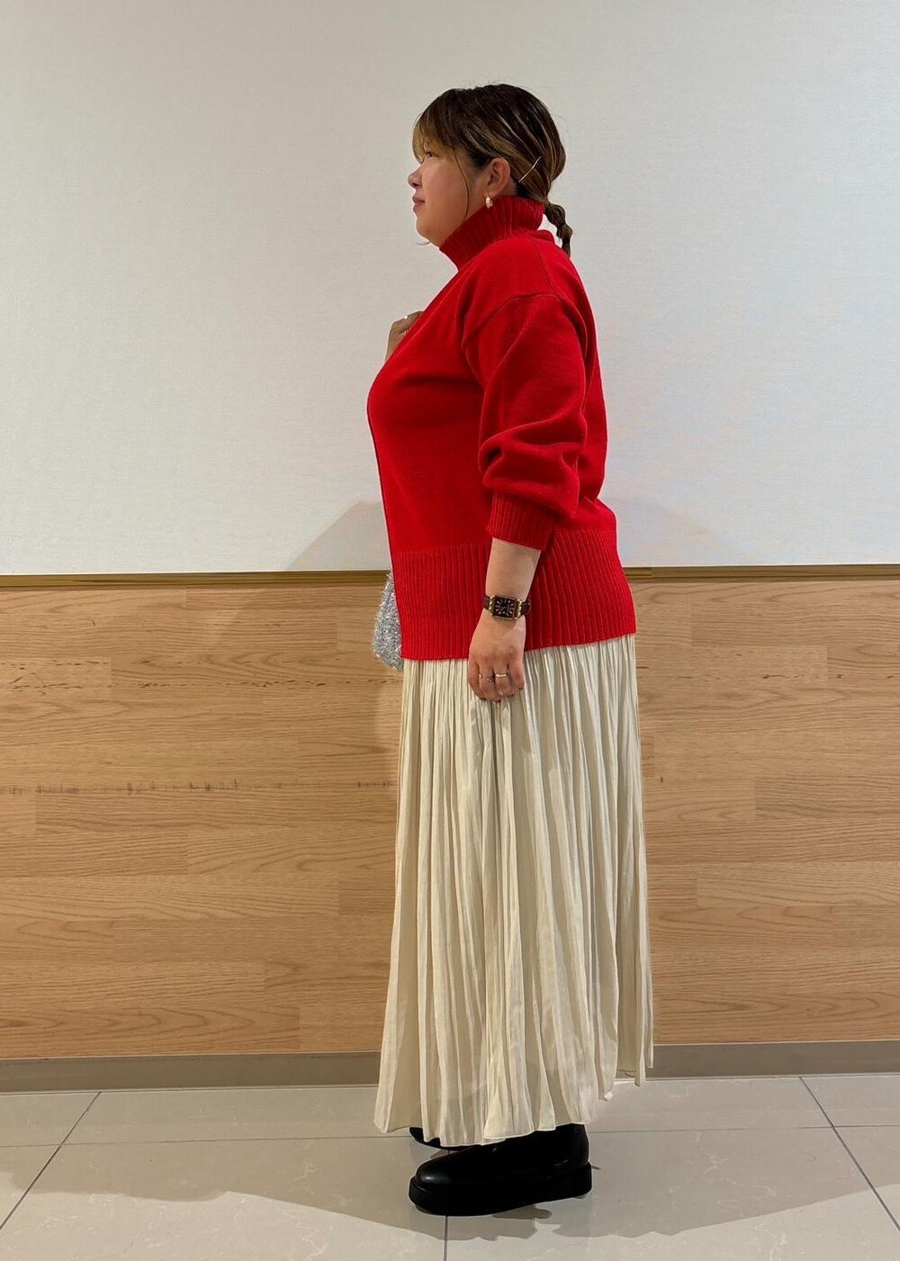 レッド系のニット/セーター、ベージュ系のスカート、ブラック系のブーツを着用したレディースの秋コーディネートの2枚目の写真