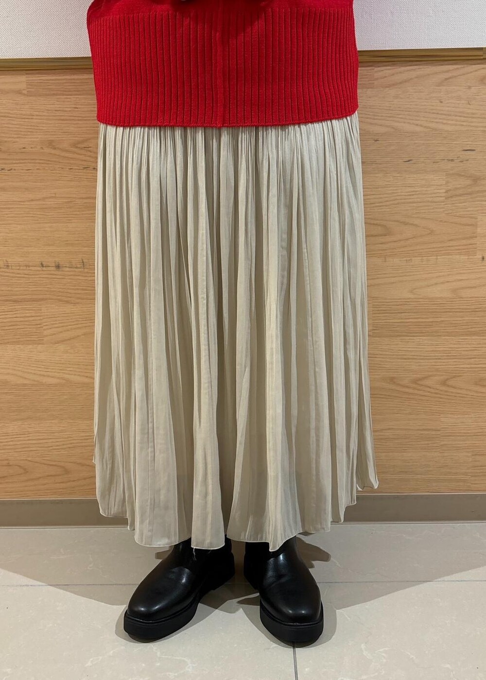 レッド系のニット/セーター、ベージュ系のスカート、ブラック系のブーツを着用したレディースの秋コーディネートの6枚目の写真