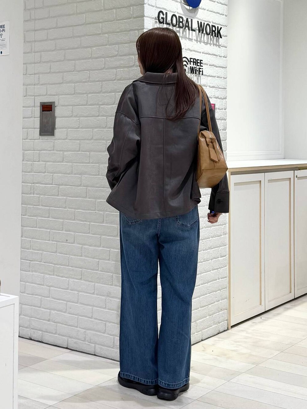 ブラウン系のボストンバッグ、ブルー系のデニムパンツ、グレー系のテーラードジャケットを着用したレディースの冬コーディネートの3枚目の写真