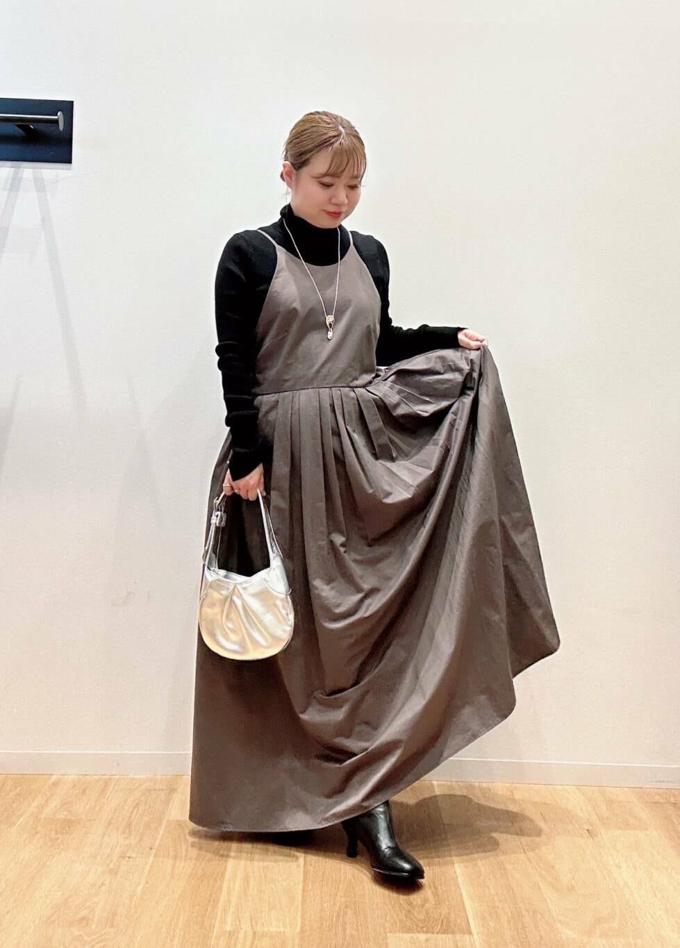 グリーン系のワンピース、ブラック系のニット/セーター、ブラック系のブーツを着用したレディースの秋コーディネートの2枚目の写真