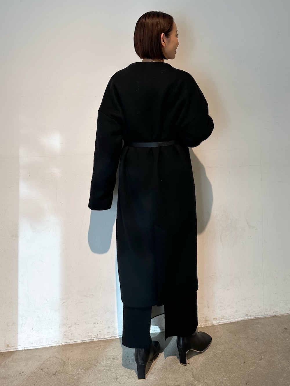 ブラック系のノーカラーコート、ブラック系のブーツ、ホワイト系のニット/セーターを着用したレディースの秋コーディネートの4枚目の写真