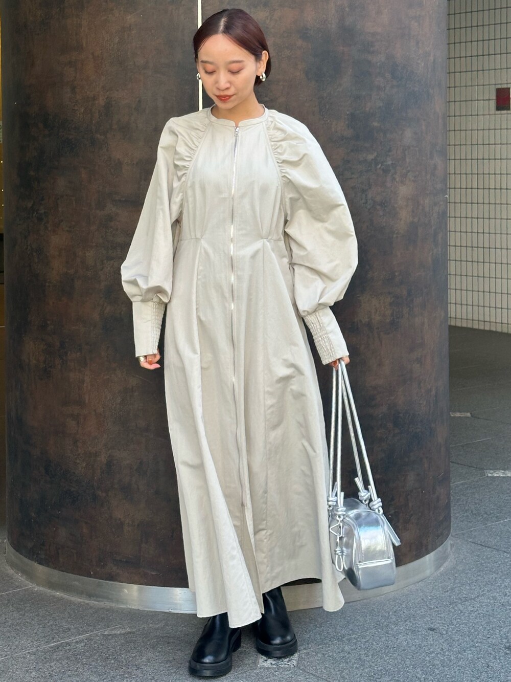 シルバー系のボストンバッグ、ブラック系のブーツ、ベージュ系のワンピースを着用したレディースの冬コーディネートの2枚目の写真