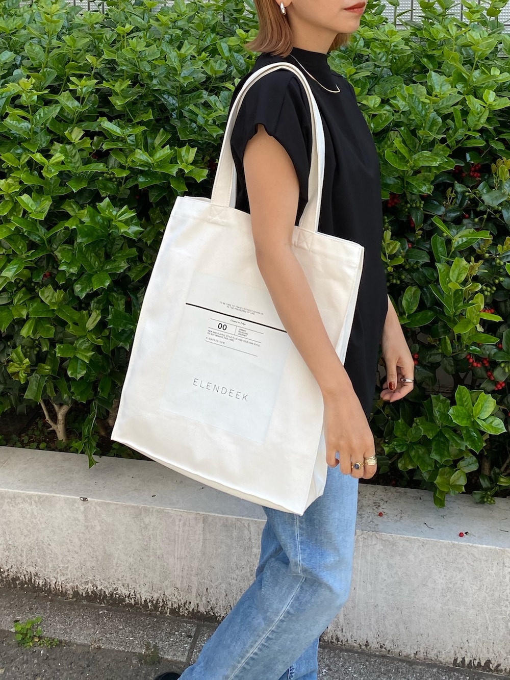 ホワイト系のトートバッグ、ブラック系のTシャツ/カットソー、ブルー系のデニムパンツを着用したレディースの春コーディネートの5枚目の写真