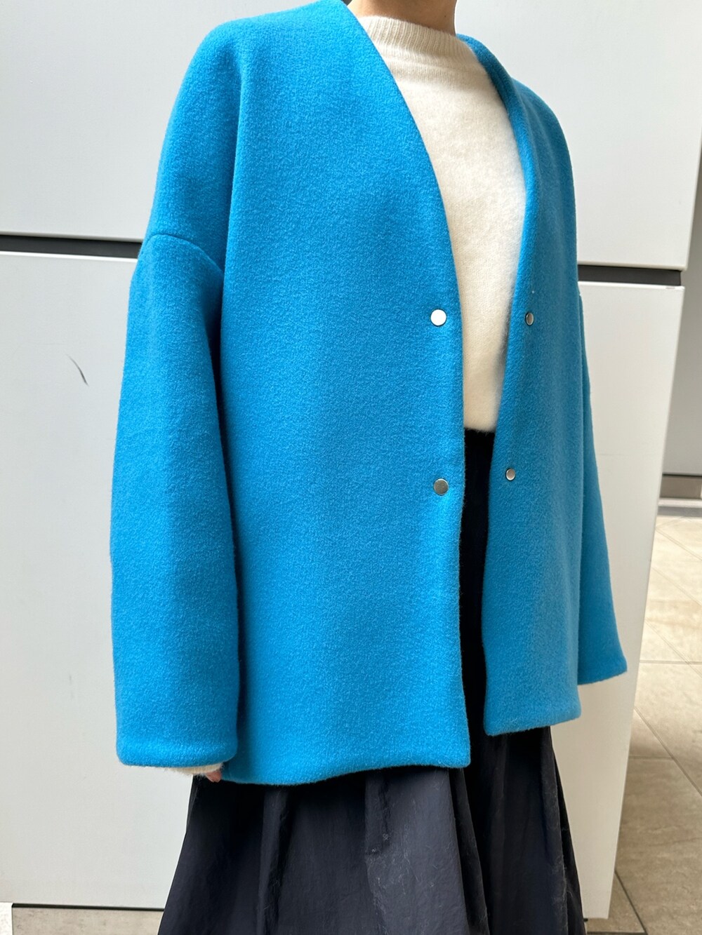 ブルー系のノーカラーコート、ブラック系のスカート、ホワイト系のニット/セーターを着用したレディースの冬コーディネートの6枚目の写真