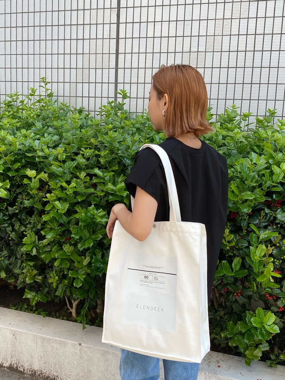 ホワイト系のトートバッグ、ブラック系のTシャツ/カットソー、ブルー系のデニムパンツを着用したレディースの春コーディネートの2枚目の写真